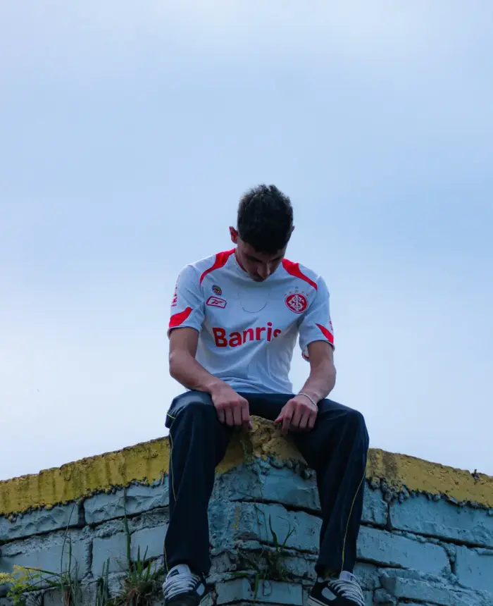 A teenage boy in a soccer jersey sitting on a wall, lost in thought